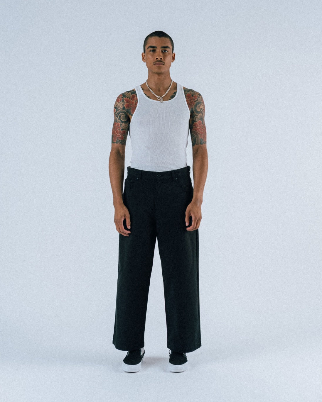 Person wearing a white tank top and black pants on a light gray background