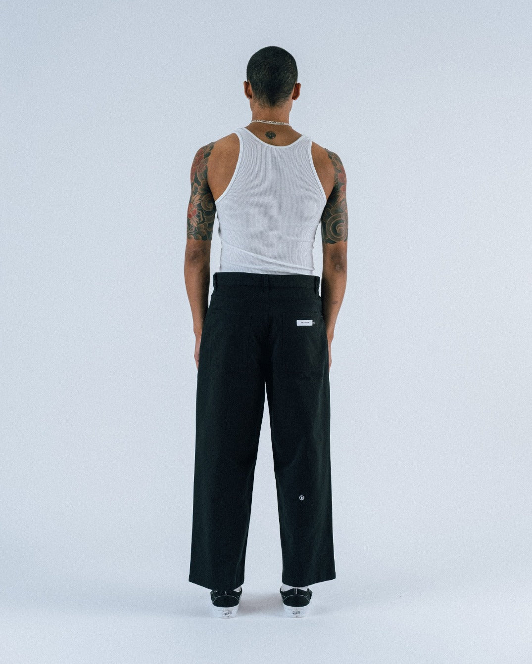 Person wearing a white sleeveless shirt and black pants on a white background