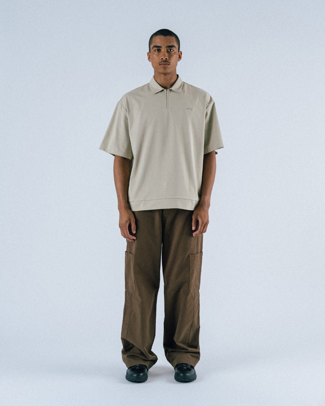 Man wearing a beige polo shirt and brown pants on a white background