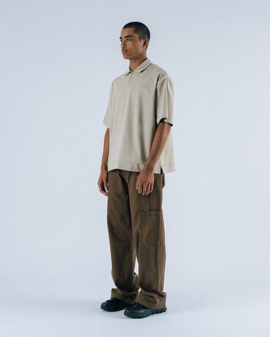 Man wearing a beige shirt and brown pants on a white background