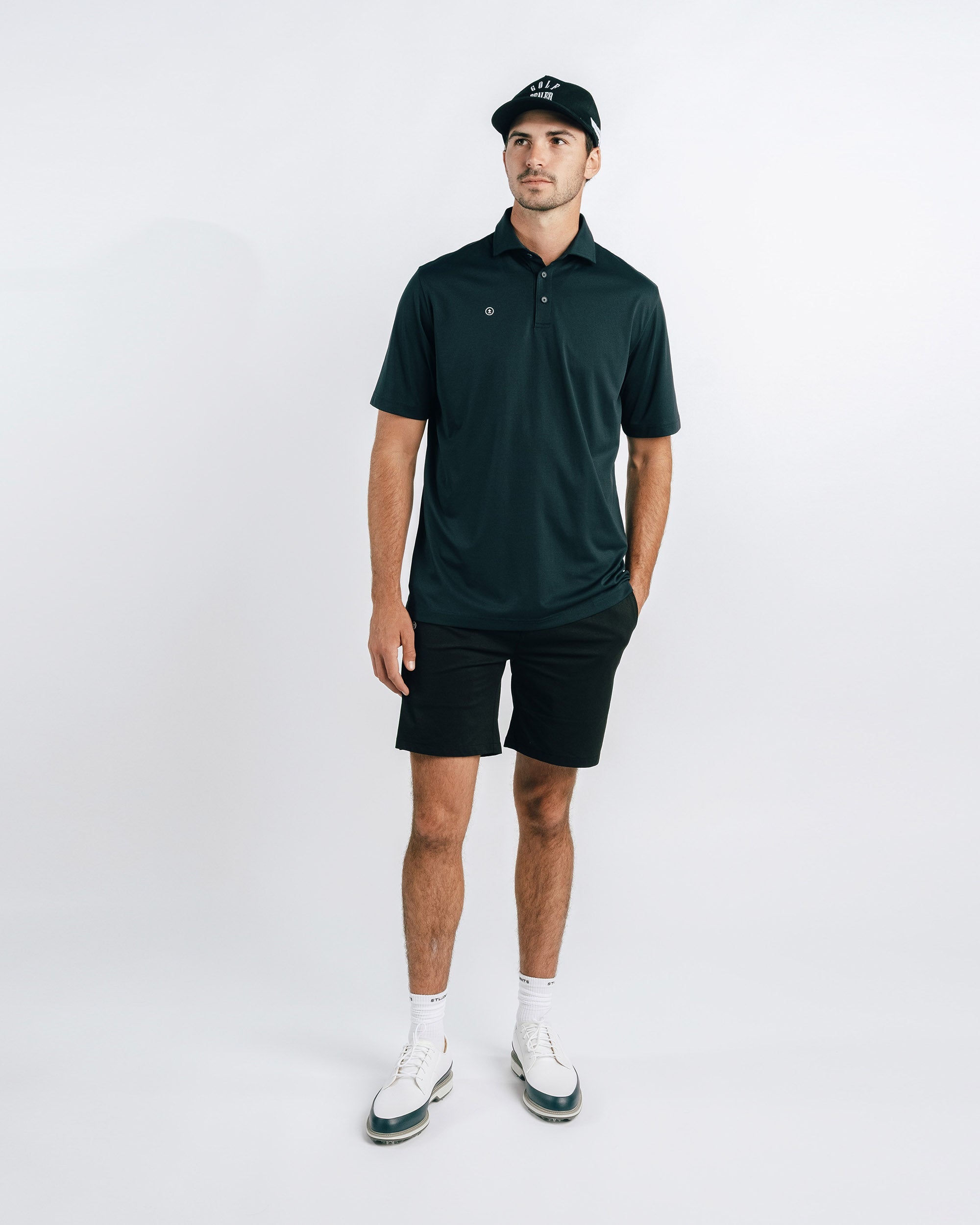 Man wearing a dark green polo shirt and black shorts on a white background