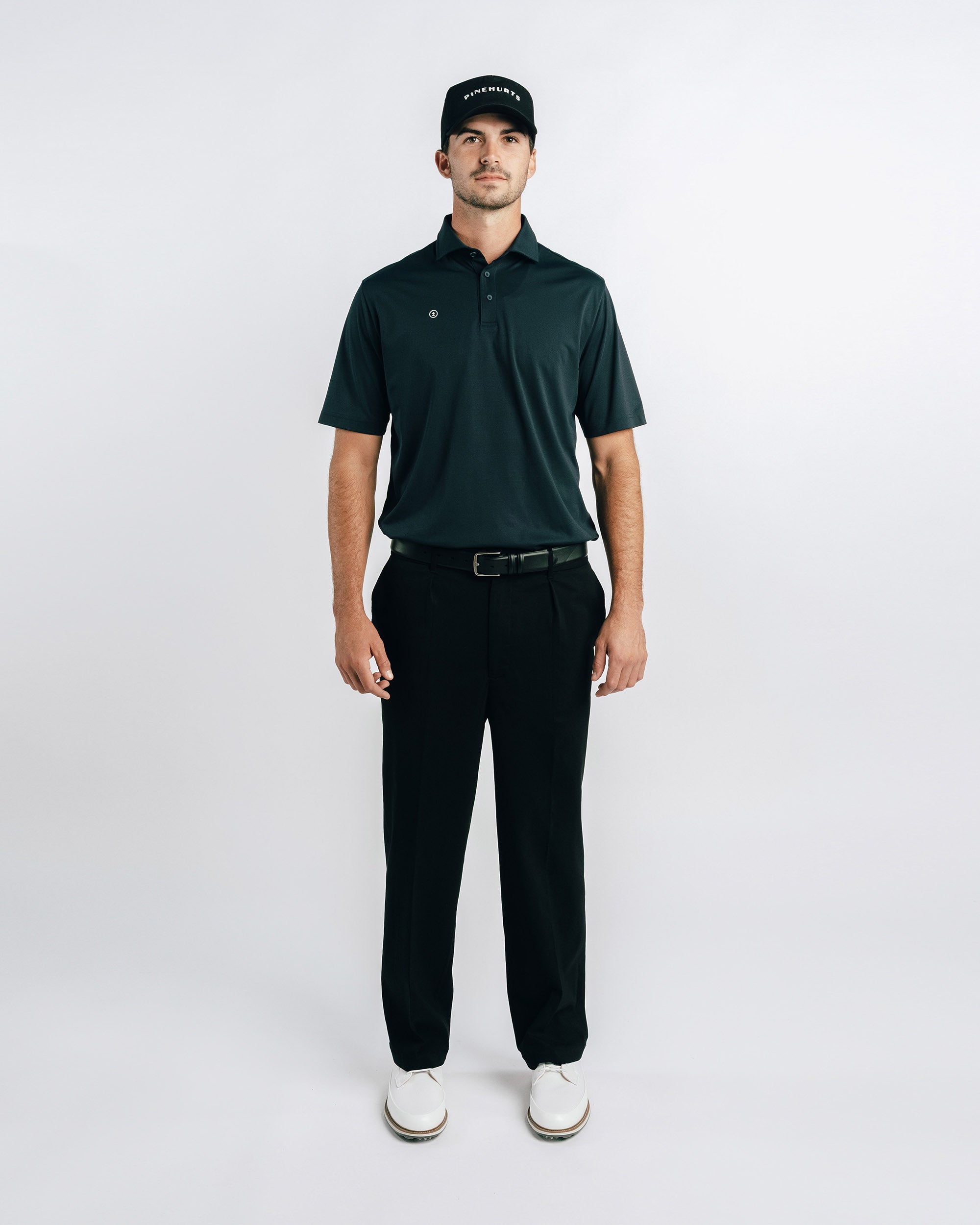 Man wearing a green polo shirt, black pants, and a cap on a white background