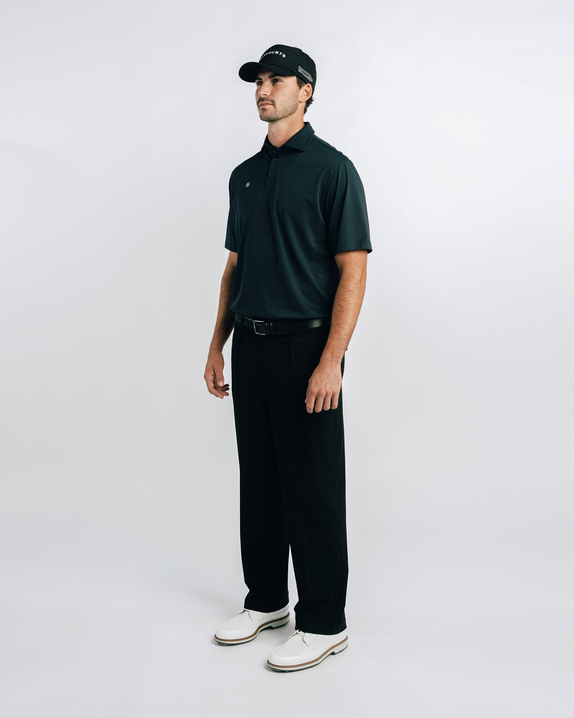 Man wearing a black polo shirt, black pants, and white shoes on a white background