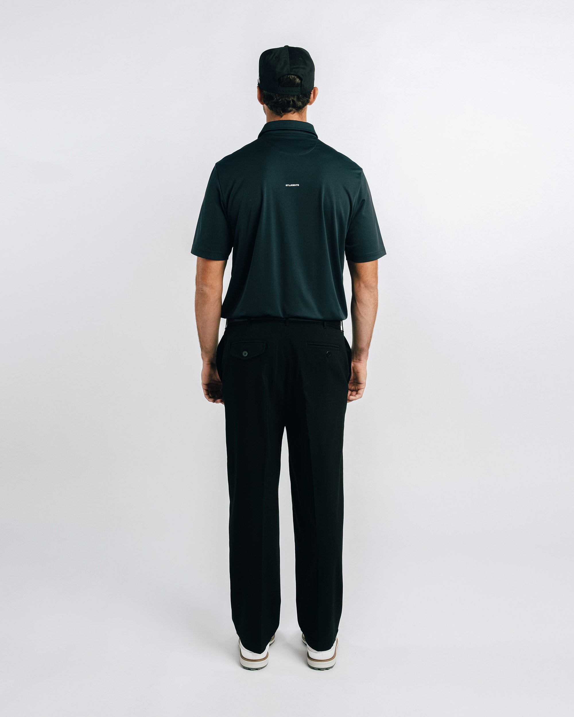 Person wearing a dark green polo shirt and black pants on a white background