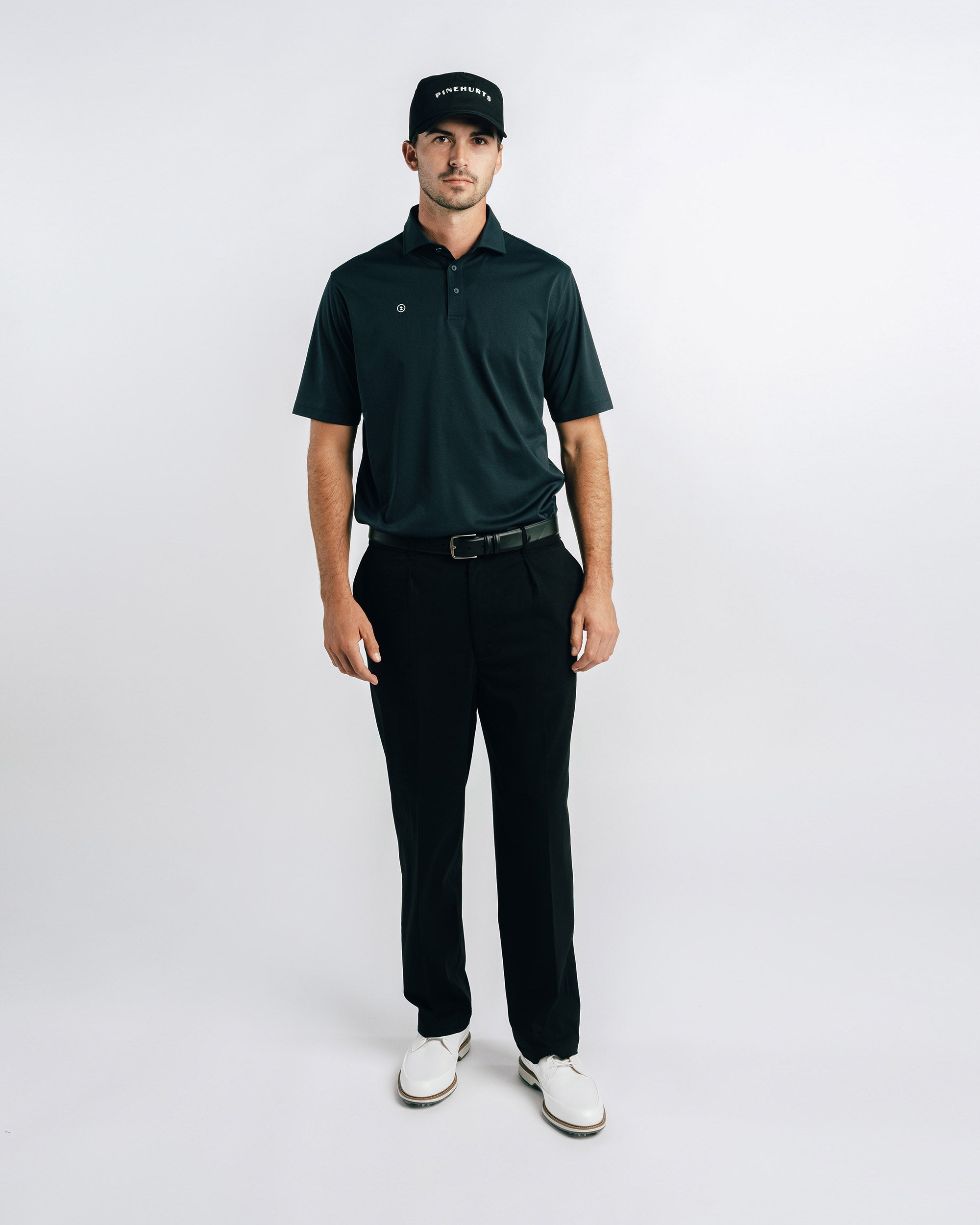 Man wearing a green polo shirt, black pants, and a black cap on a white background