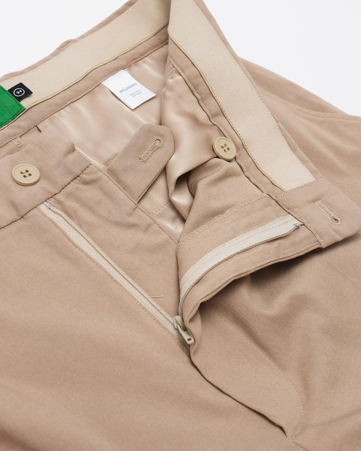 Close-up of beige pants with a brand tag on a white background