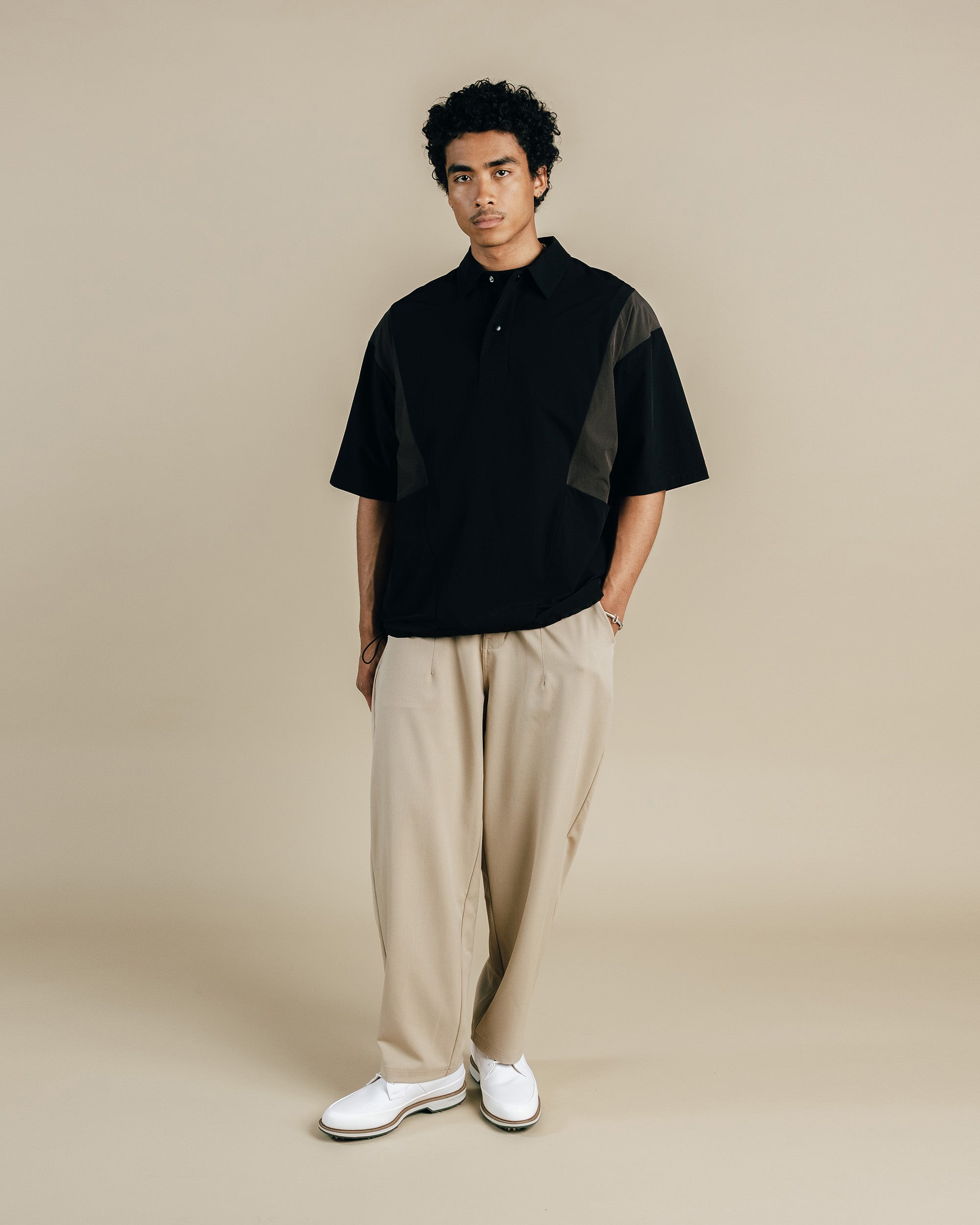 Man wearing a black and brown shirt with beige pants on a beige background