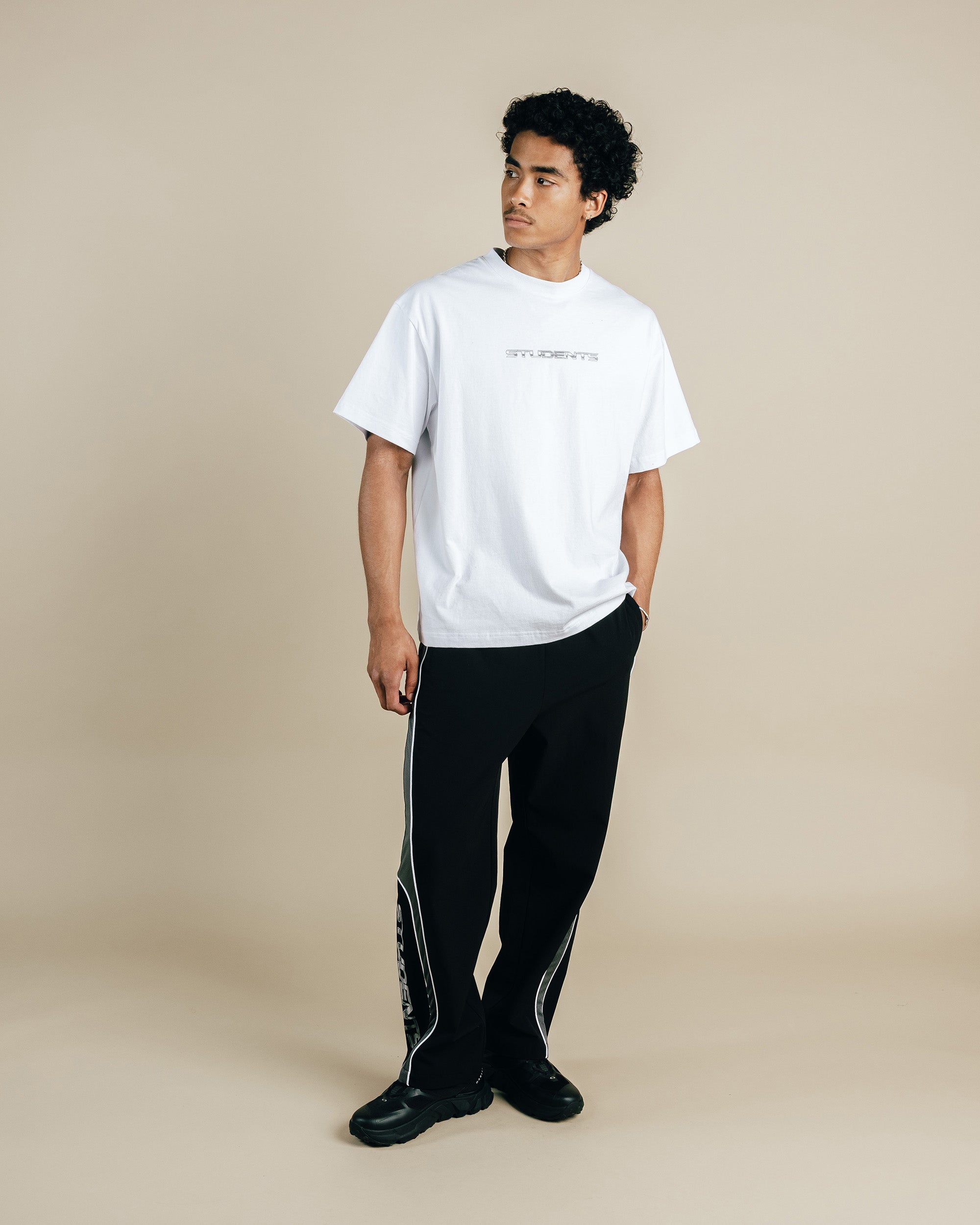 Person wearing a white t-shirt and black pants on a beige background