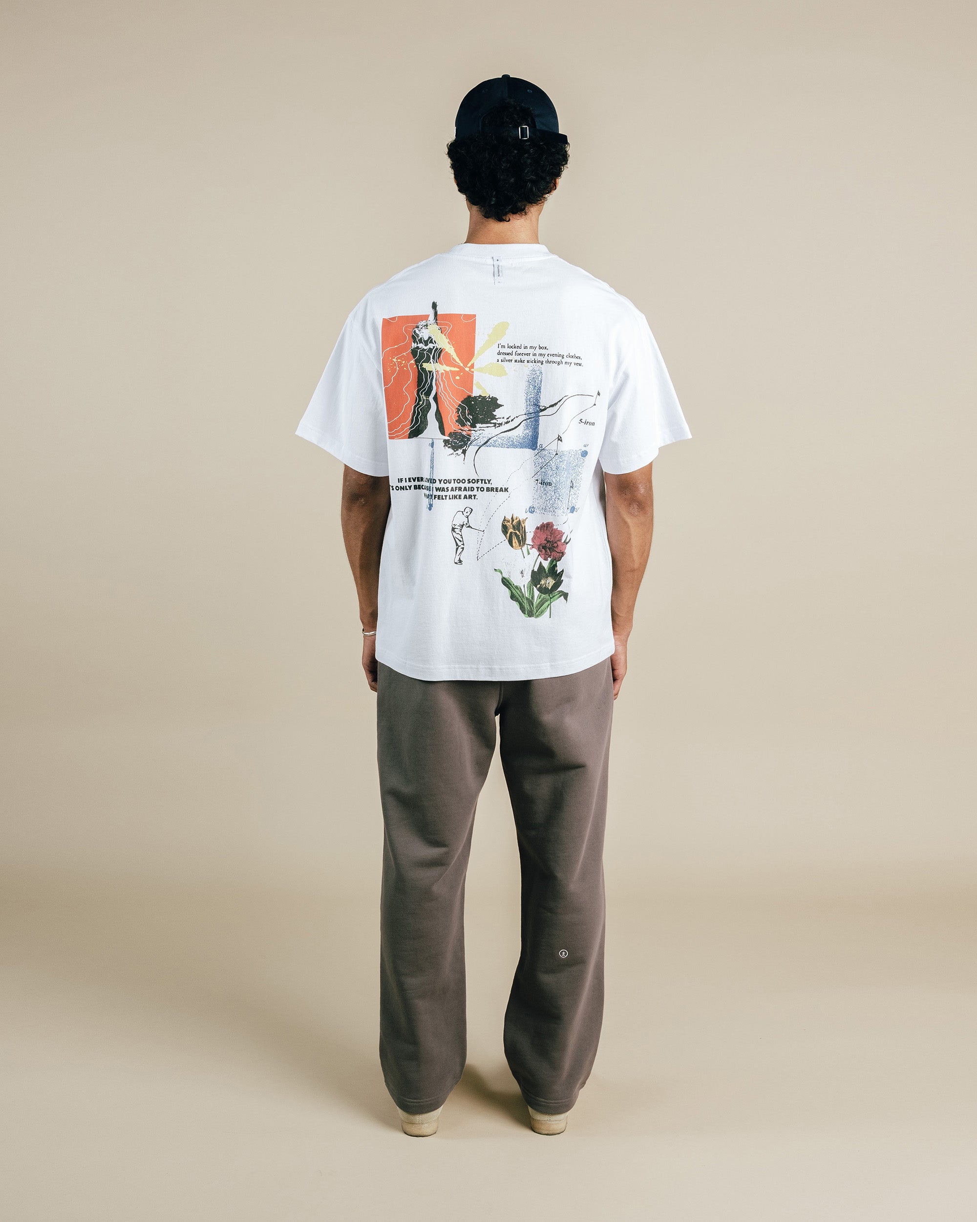 Person wearing a white t-shirt with a graphic design on the back, standing against a beige background