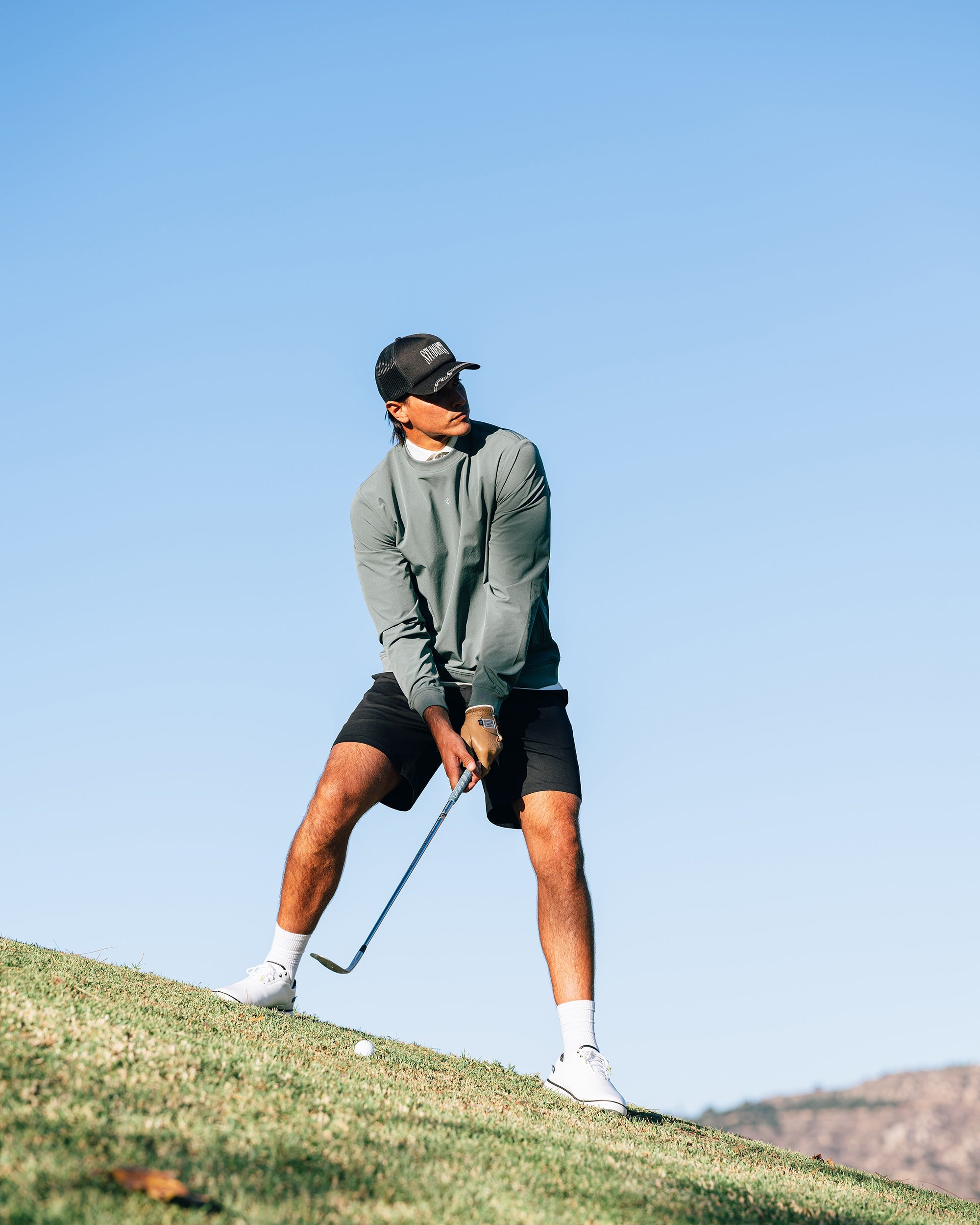 Person playing golf on a grassy area with a clear blue sky