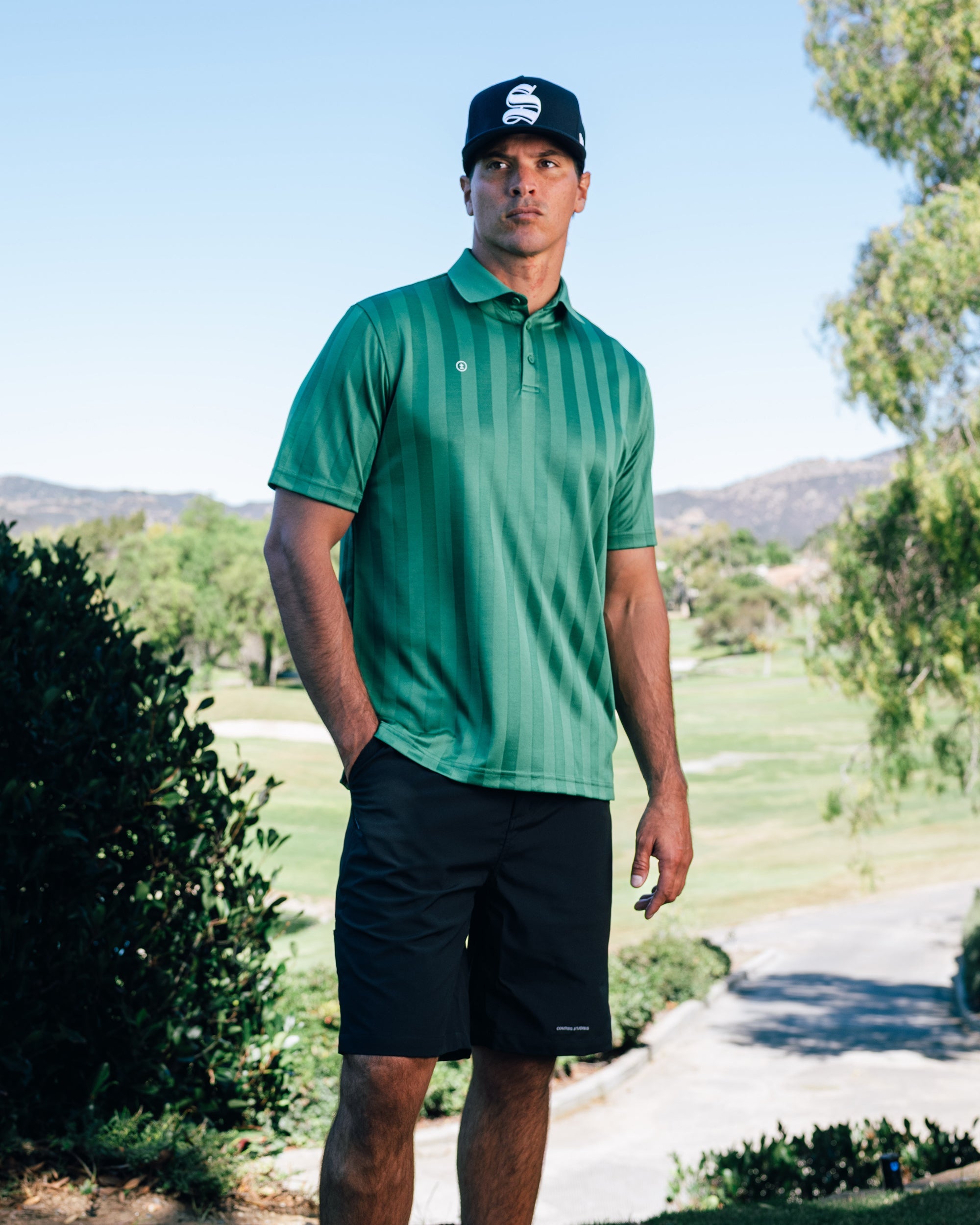 Man wearing a green polo shirt and black cap on a golf course
