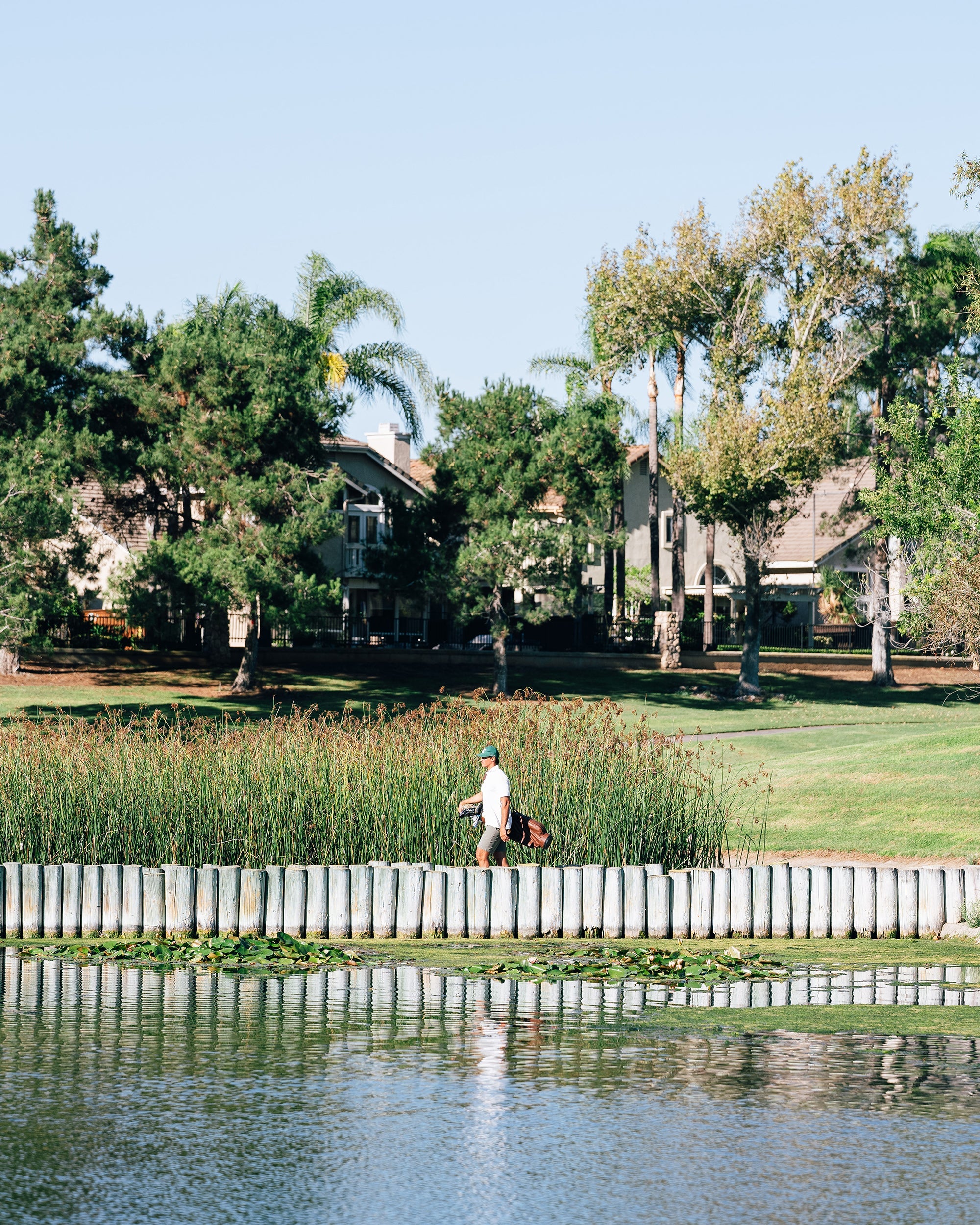 Person fishing by a lake with trees and houses in the background