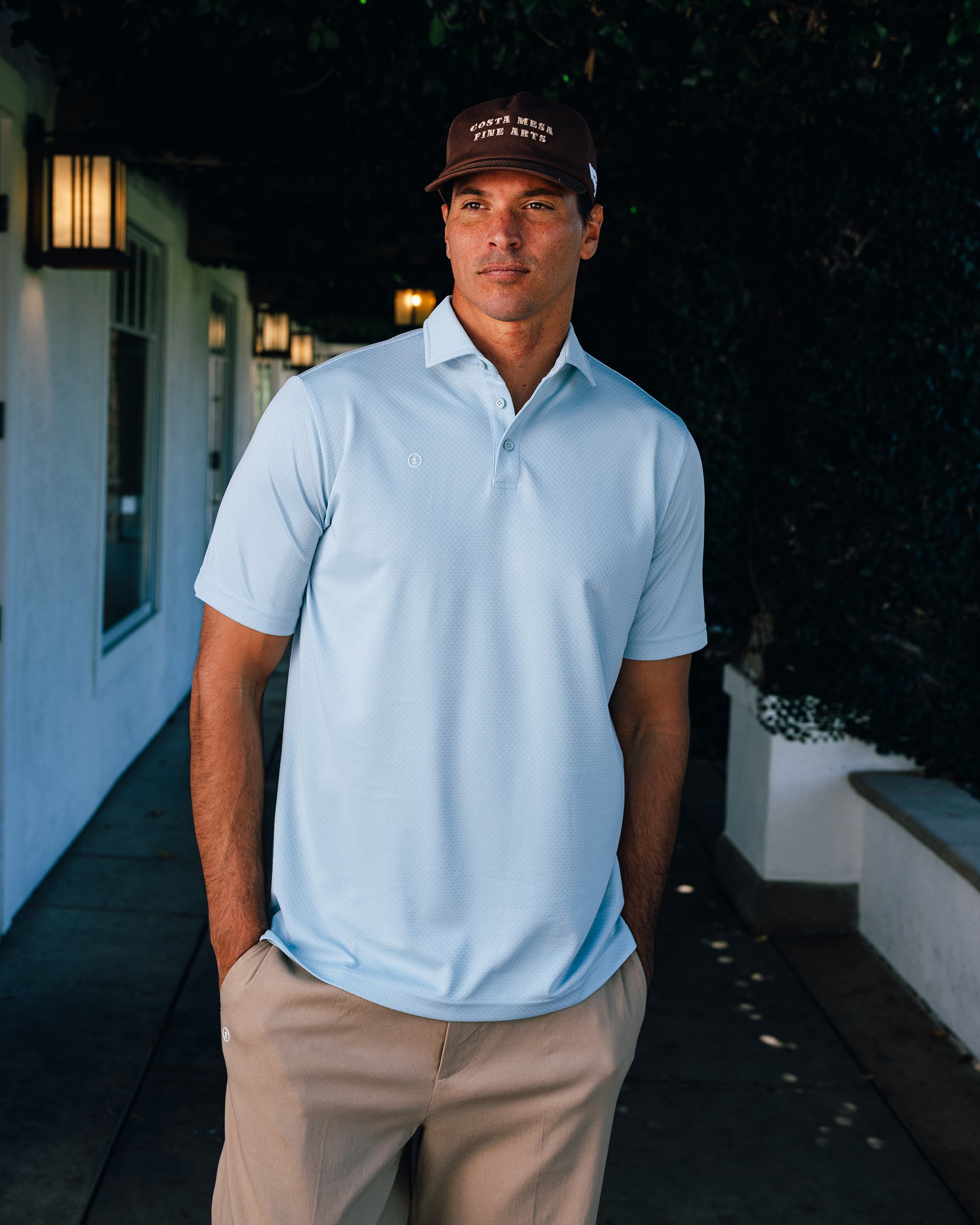 Man wearing a light blue polo shirt and beige pants standing outdoors.