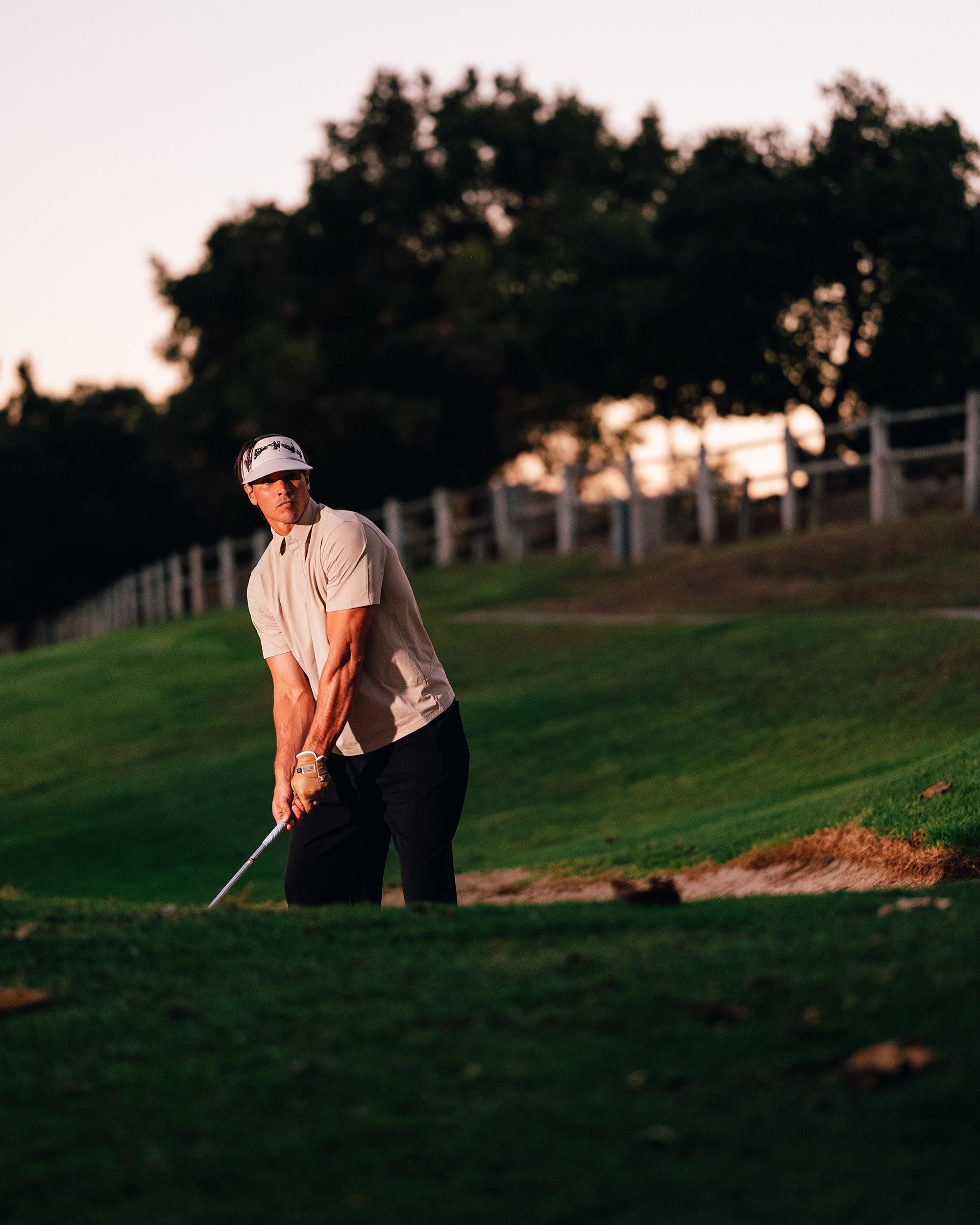 Golfer taking a swing on a golf course with trees and sunset in the background