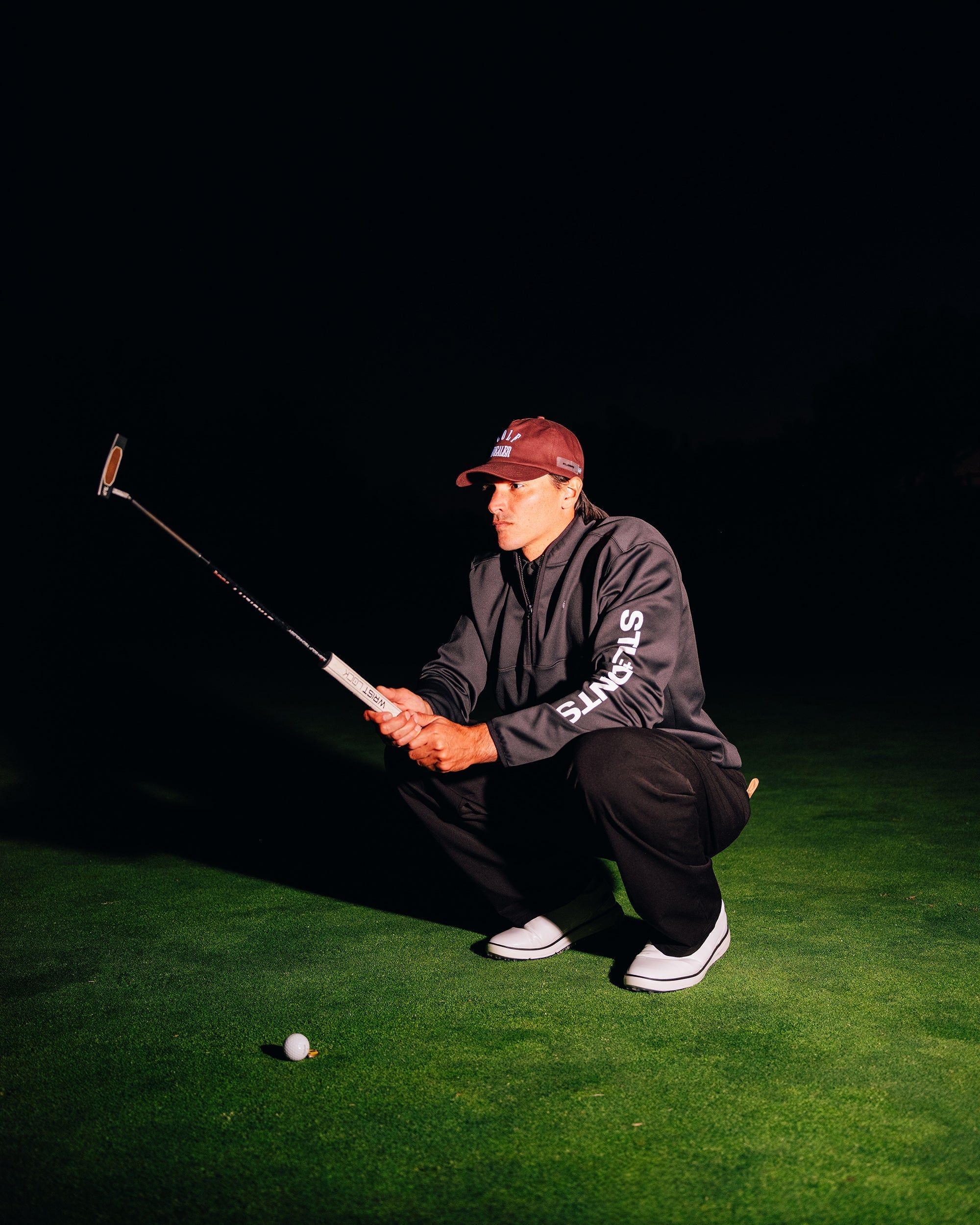 Person preparing to take a golf swing on a green surface with a dark background