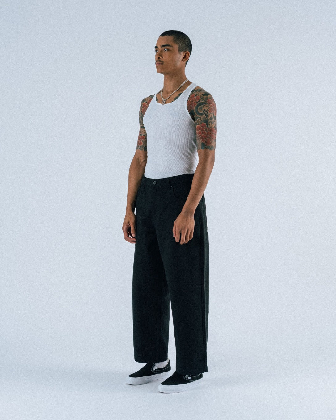 Man wearing a white tank top and black pants on a white background