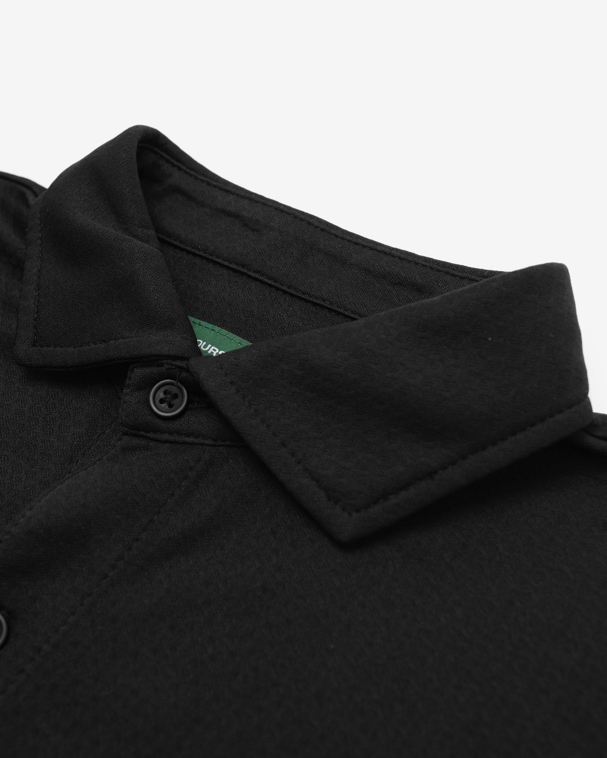 Close-up of a black shirt collar with a brand logo on a white background