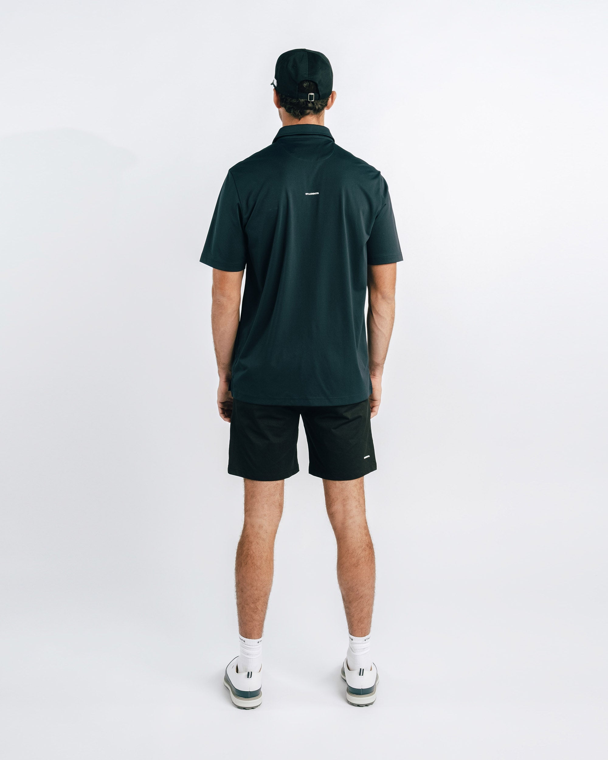 Person wearing a dark green polo shirt and black shorts on a white background