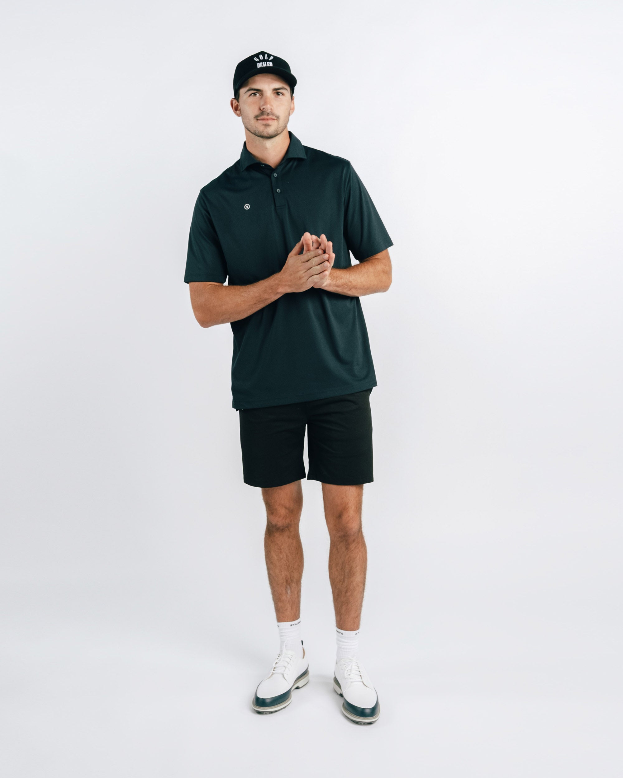 Man wearing a dark green polo shirt and black shorts on a white background