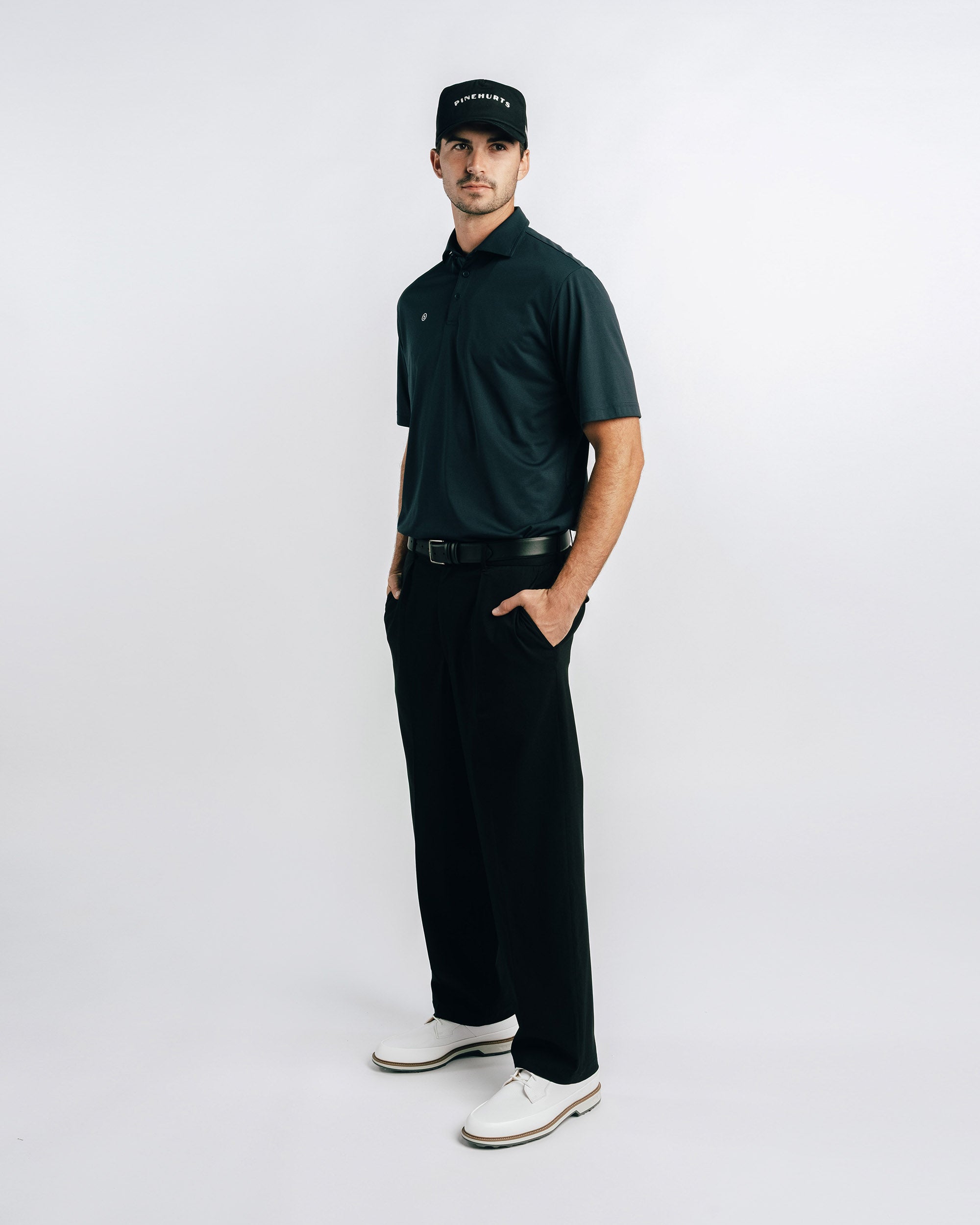 Man wearing a black polo shirt, pants, and cap on a white background