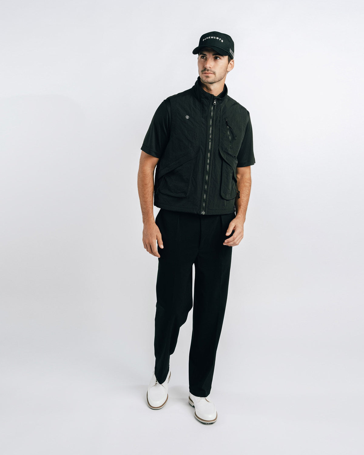 Man wearing a black outfit with a vest and cap on a white background