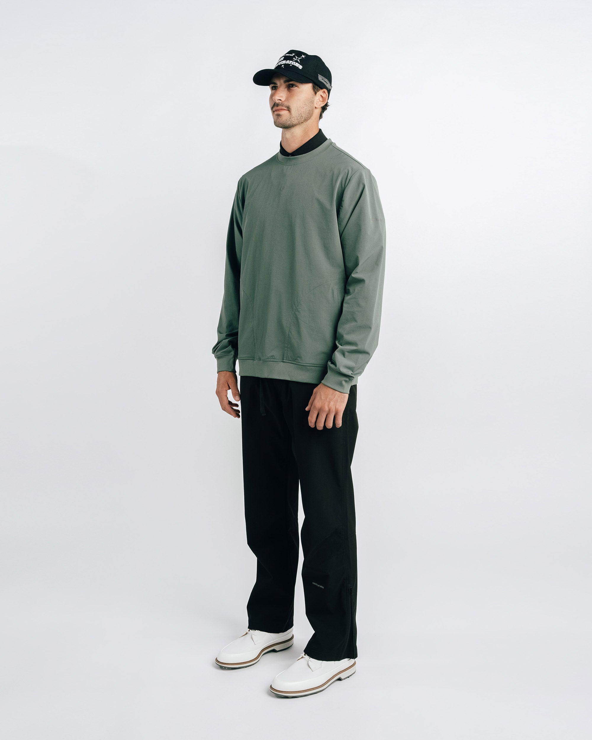 Man wearing a green sweater and black pants on a white background