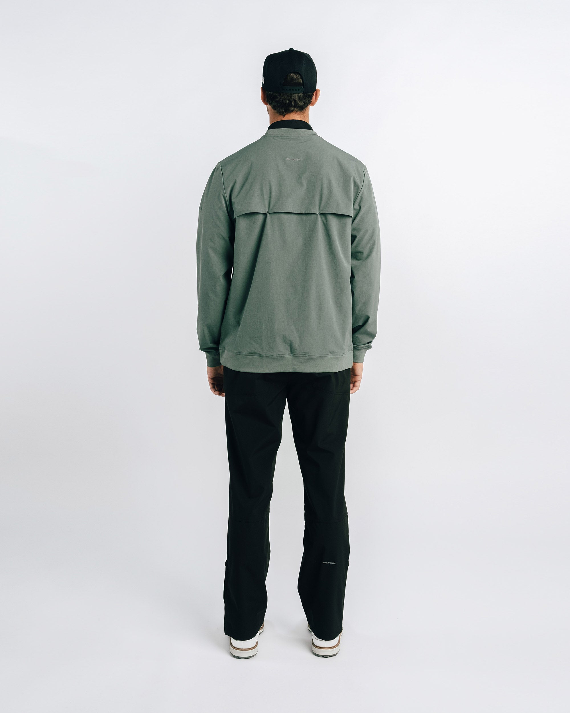 Person wearing a green jacket and black pants on a white background