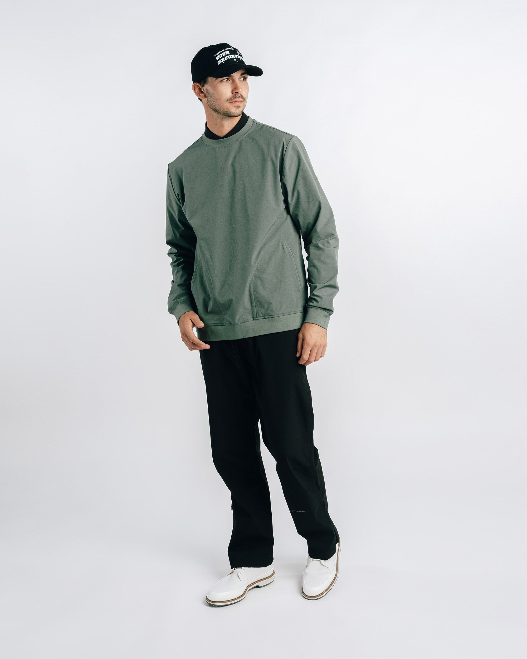 Man wearing a green sweatshirt, black pants, and a black cap on a white background