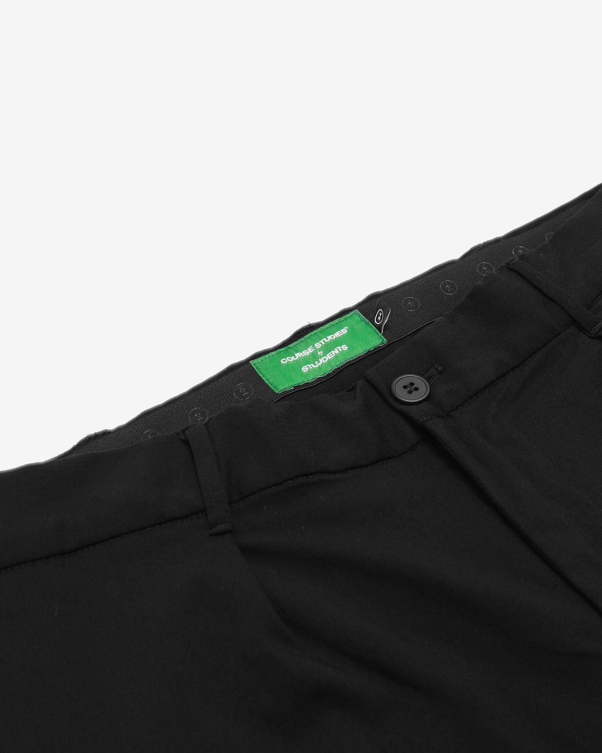 Close-up of black pants with a green label on a white background