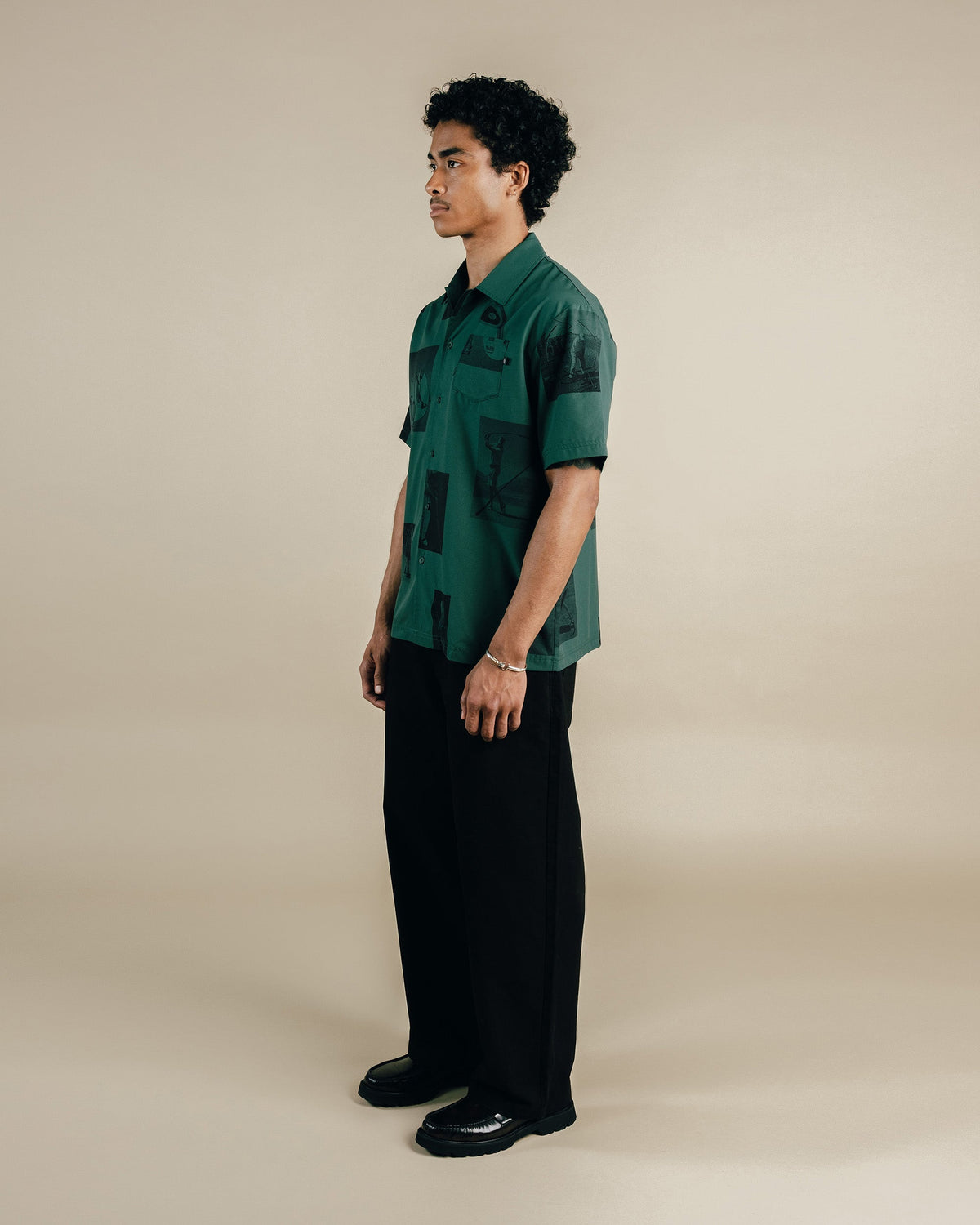 Man wearing a green patterned shirt and black pants on a beige background