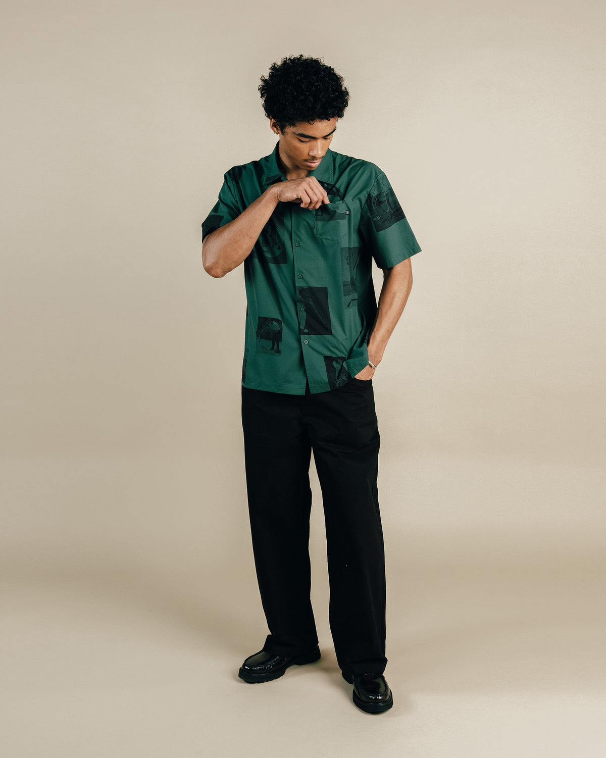Man wearing a green patterned shirt and black pants on a beige background