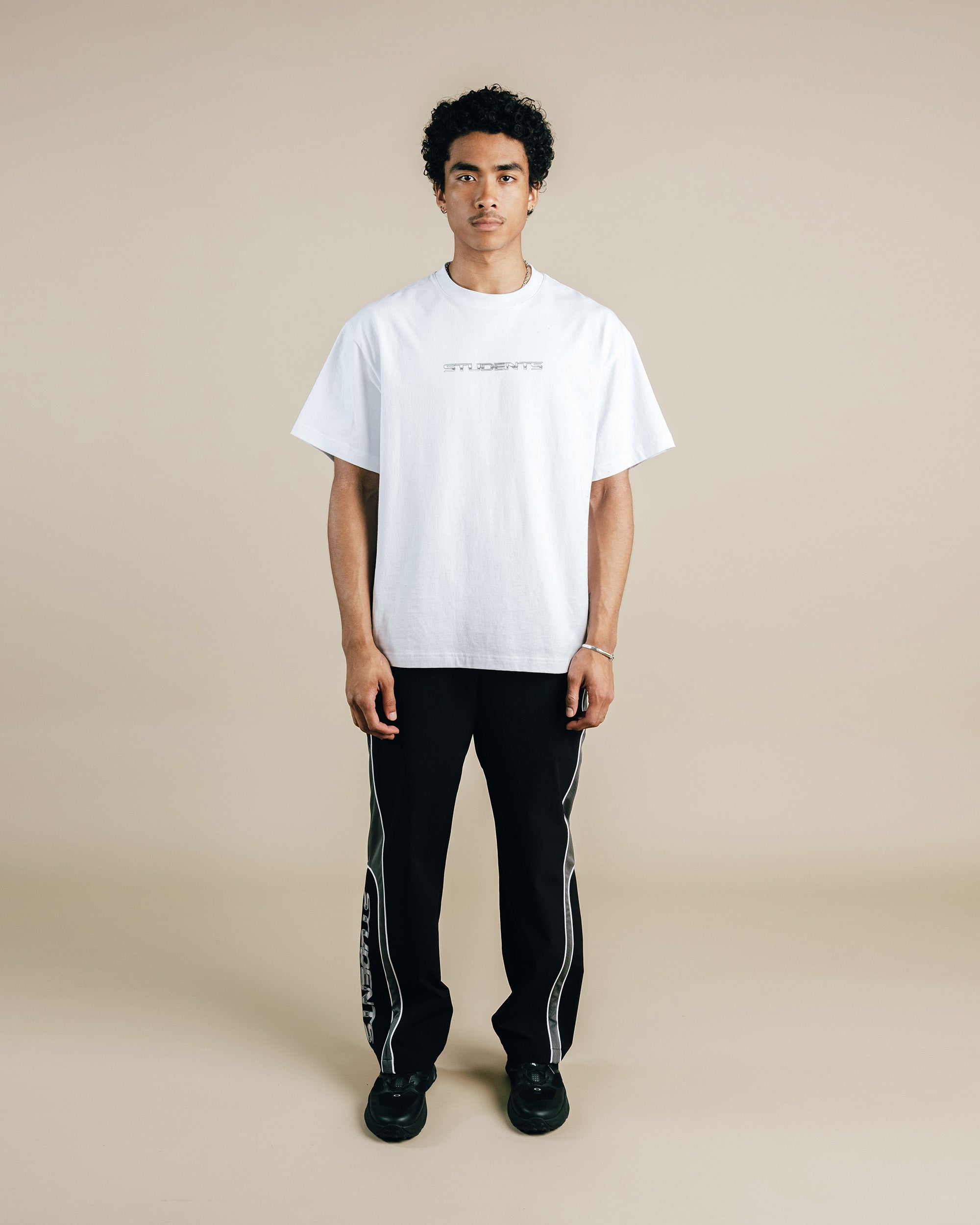Person wearing a white t-shirt and black pants with white stripes on a beige background