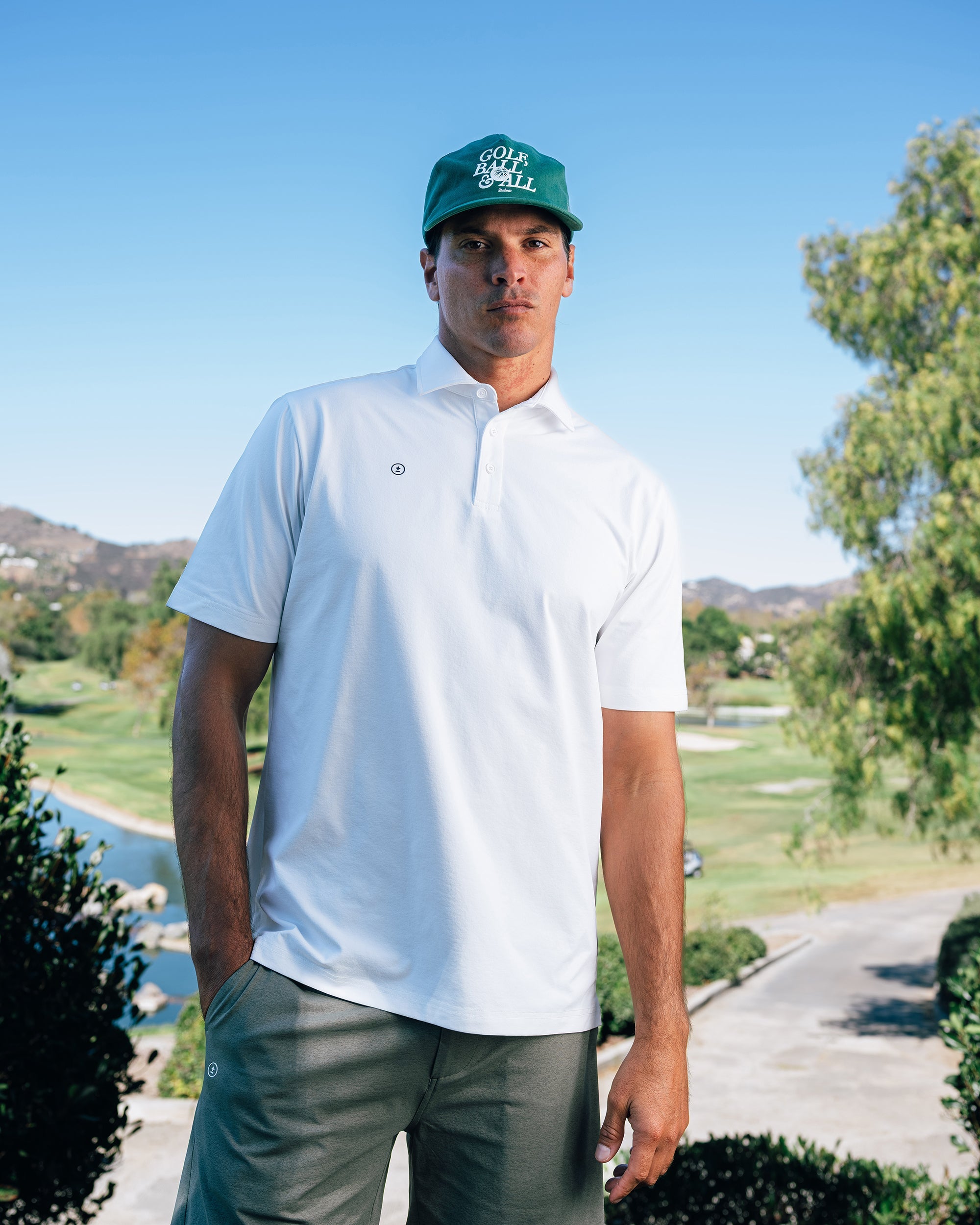 Man wearing a white polo shirt and green cap on a golf course