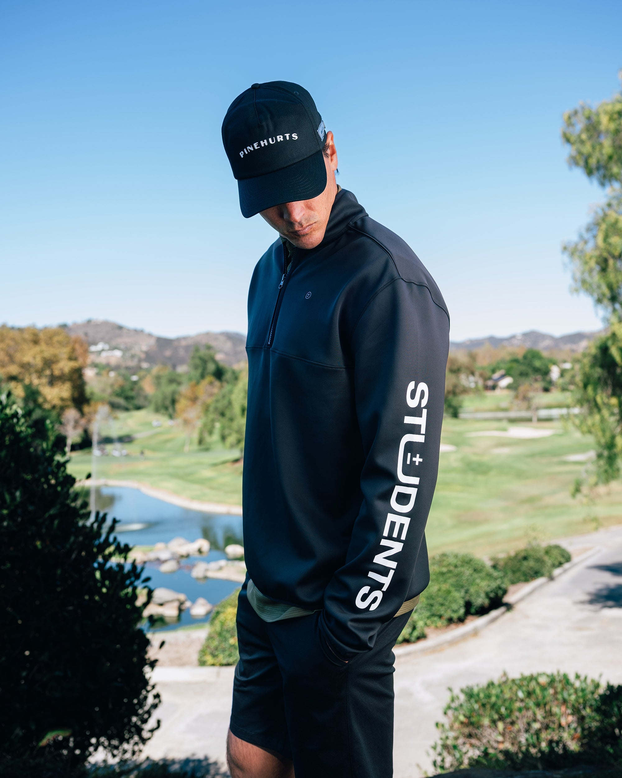 Person wearing a dark jacket with 'STUDENTS' text outdoors on a golf course