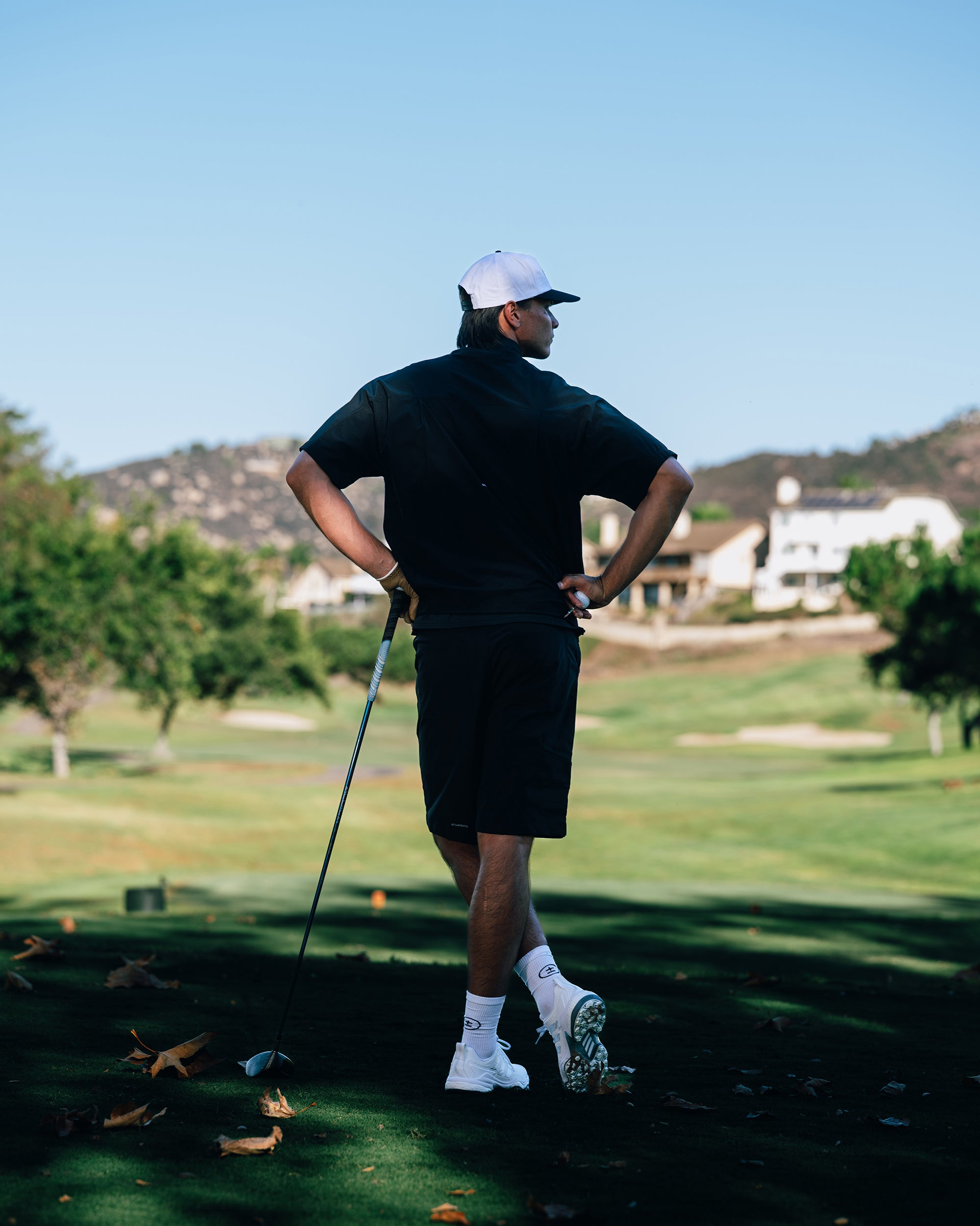 Man playing golf on a sunny day with houses and trees in the background