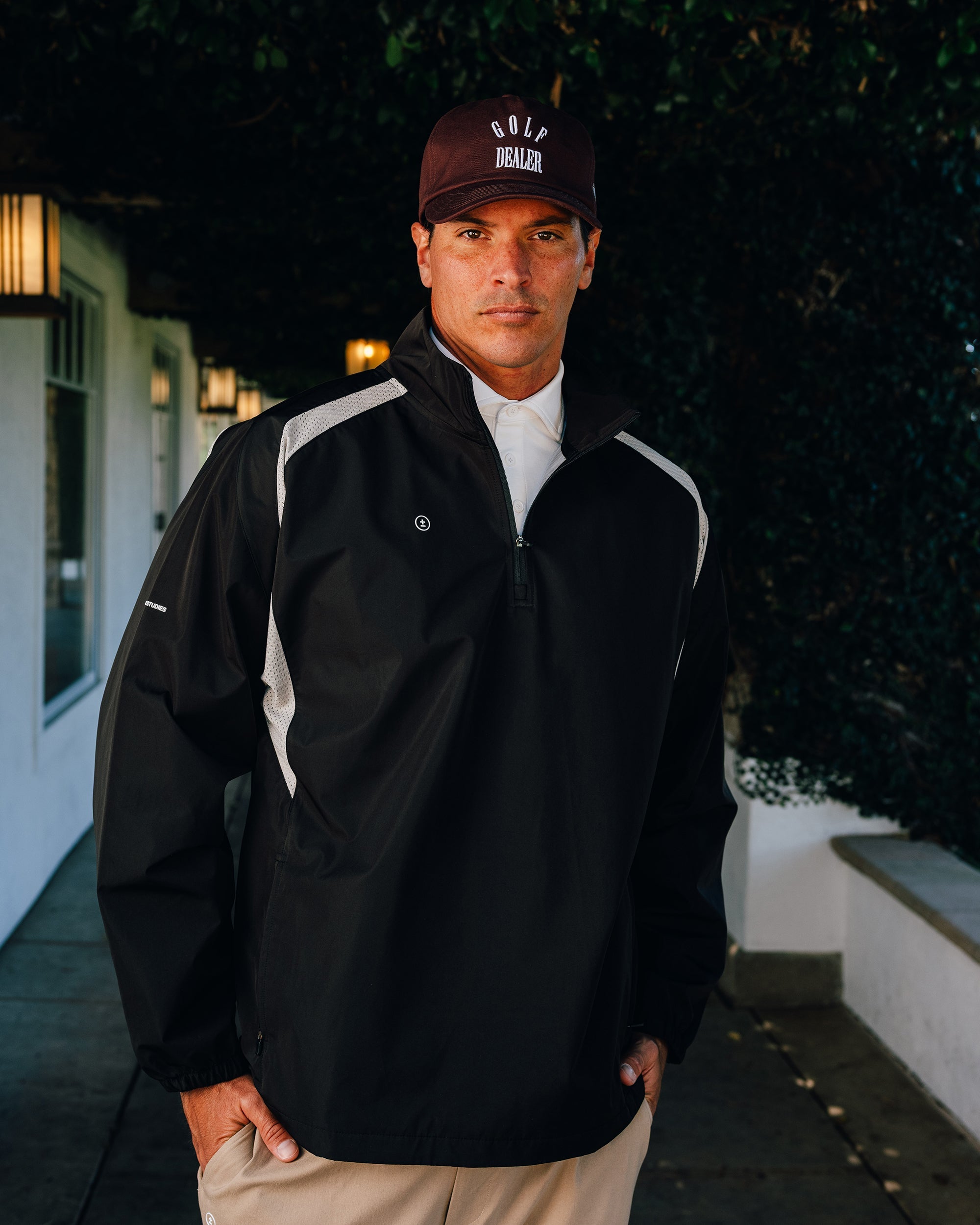 Man wearing a black jacket and cap with 'Wolf Den' logo outdoors.